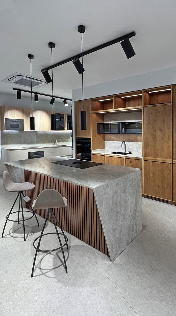 Isla de cocina con frente de madera, encimera de piedra y taburetes en la exposición de cocinas de Ferrolan Santa Coloma